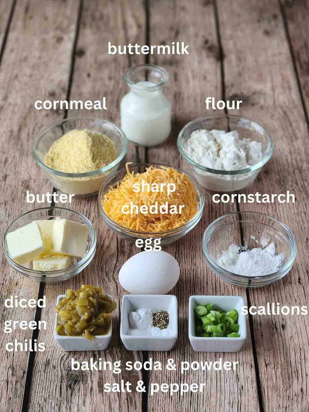Labeled ingredients in small bowls for savory waffles on a wood surface.