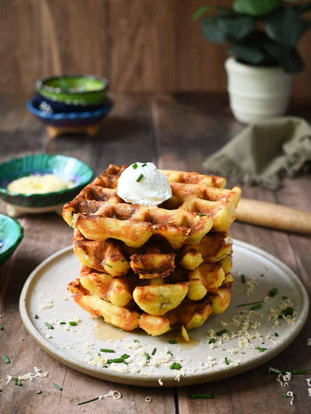 A stack of savory waffles on brown plate with small bowls in the back.