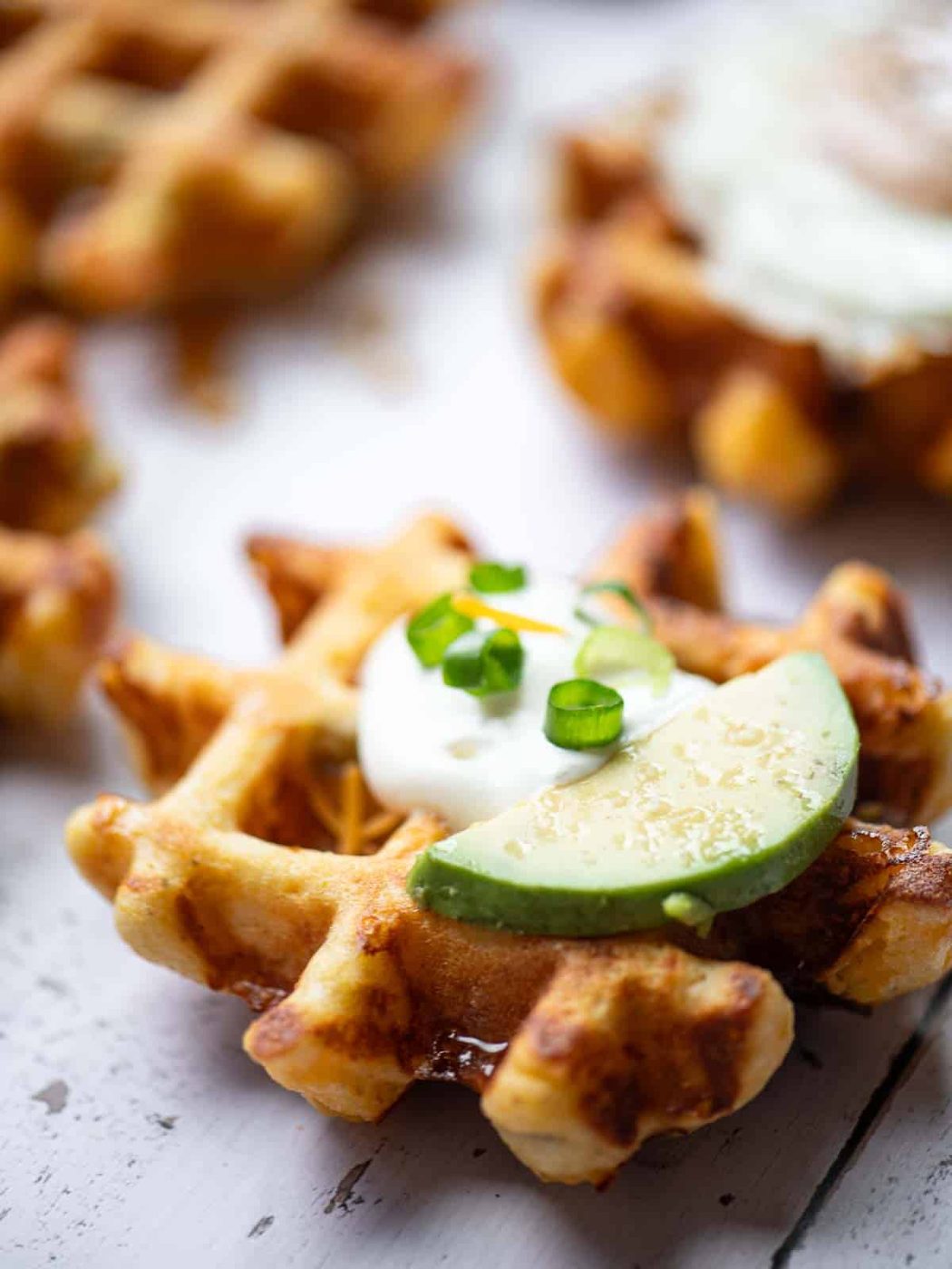 Close up of a waffle with sour cream and sliced avocado on top.
