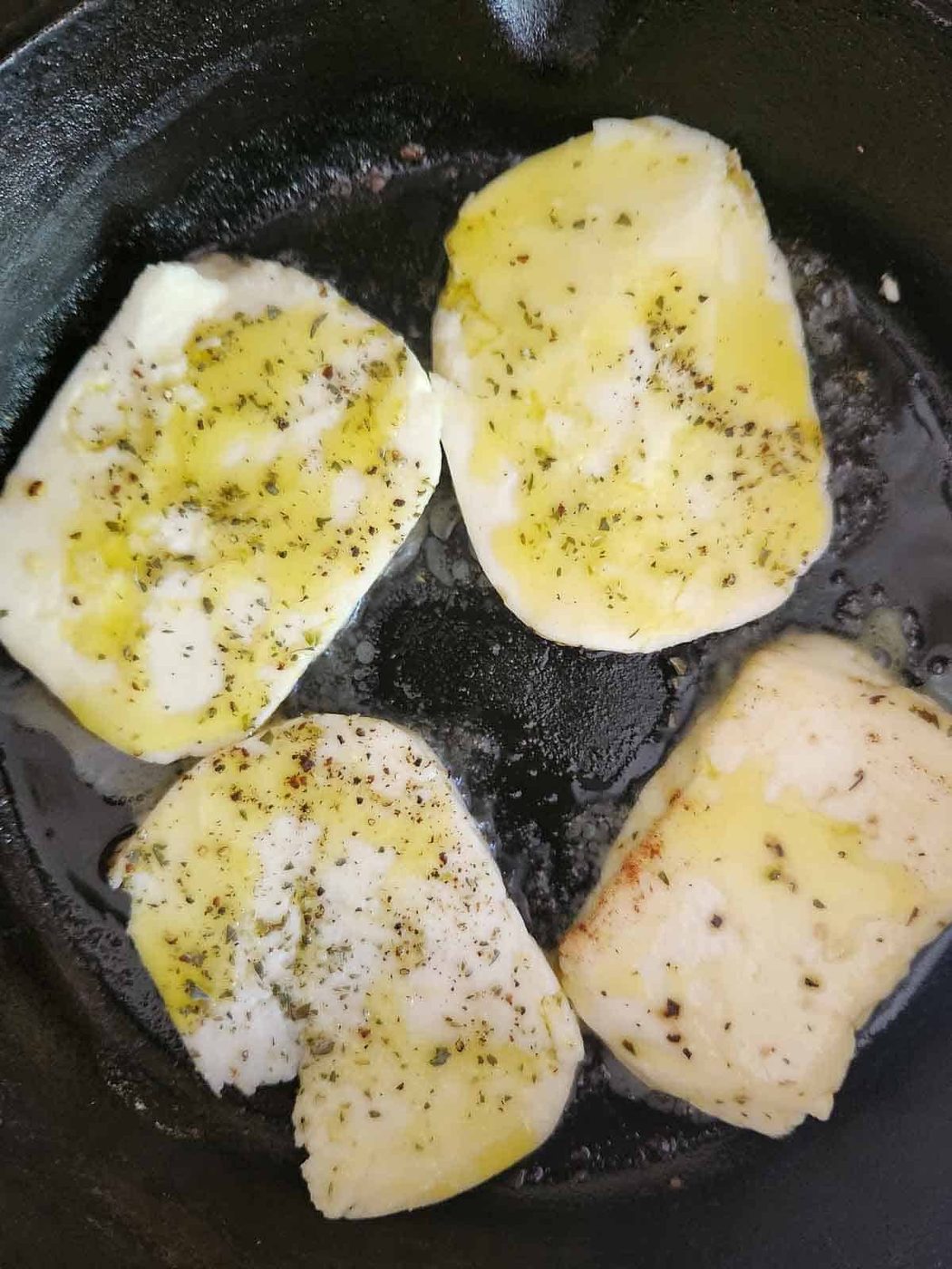 Halloumi cheese in a black skillet with oil.