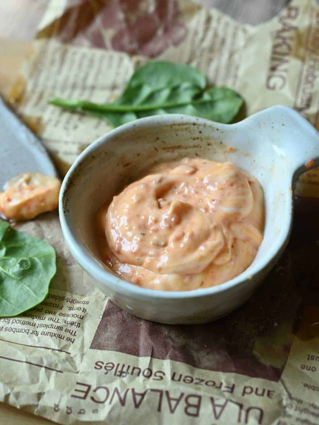 Red pepper pesto aioli in a small bowl on parchment paper with a knife in the background.