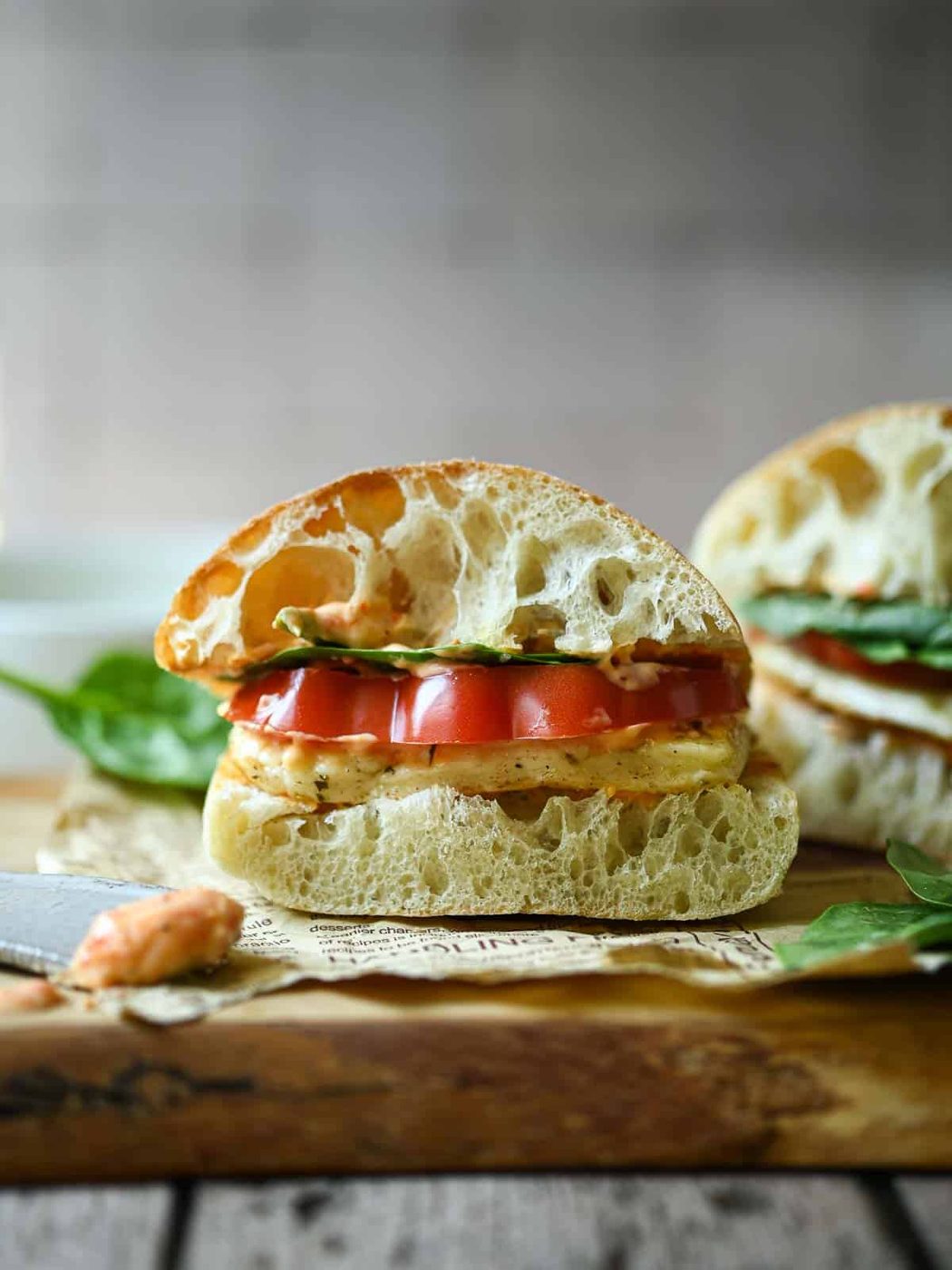 Eye-level view of a halloumi sandwich on a wood surface with a second sandwich in the background.