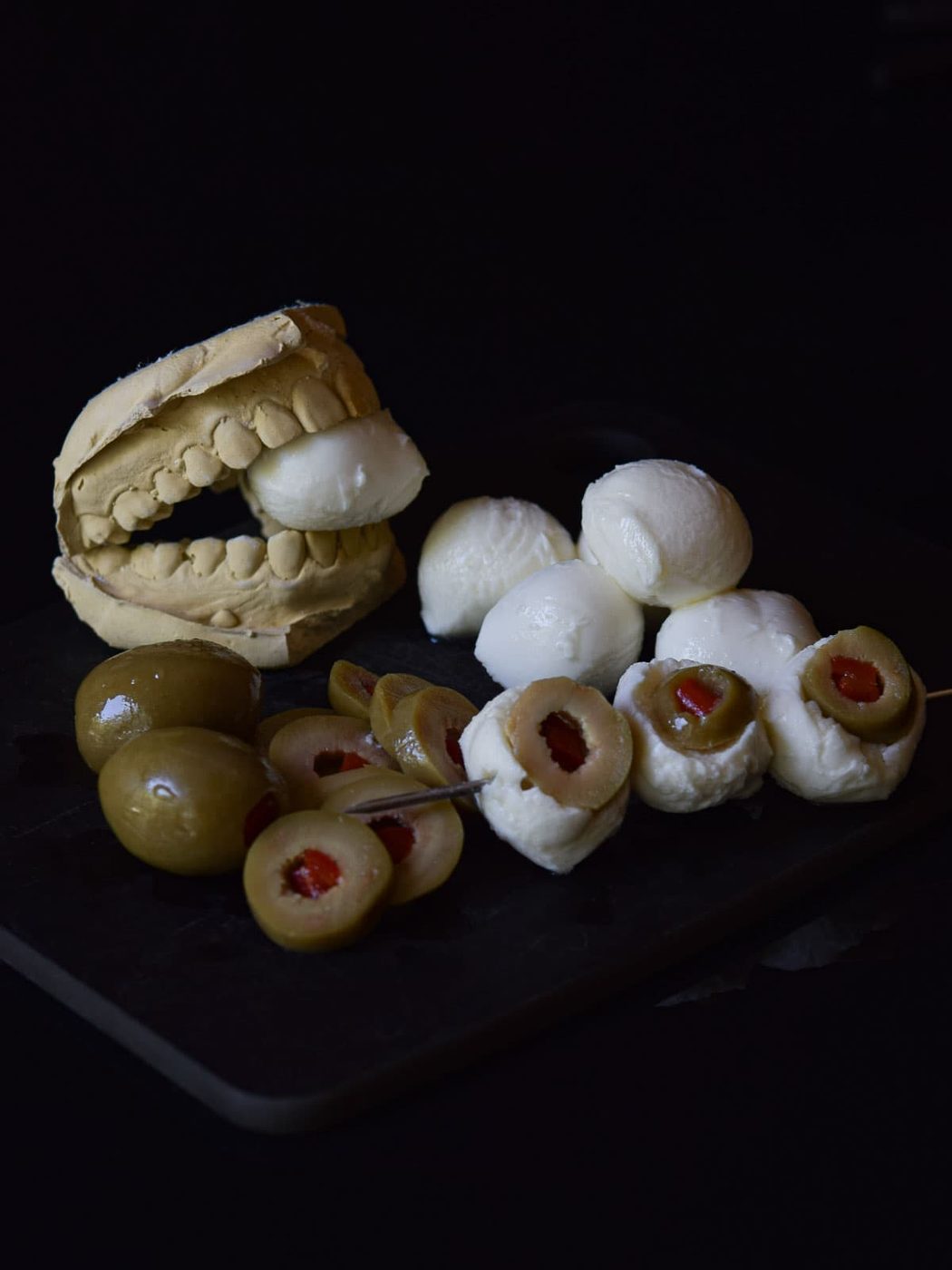 Mozzarella eyeballs on a skewer on a black surface.