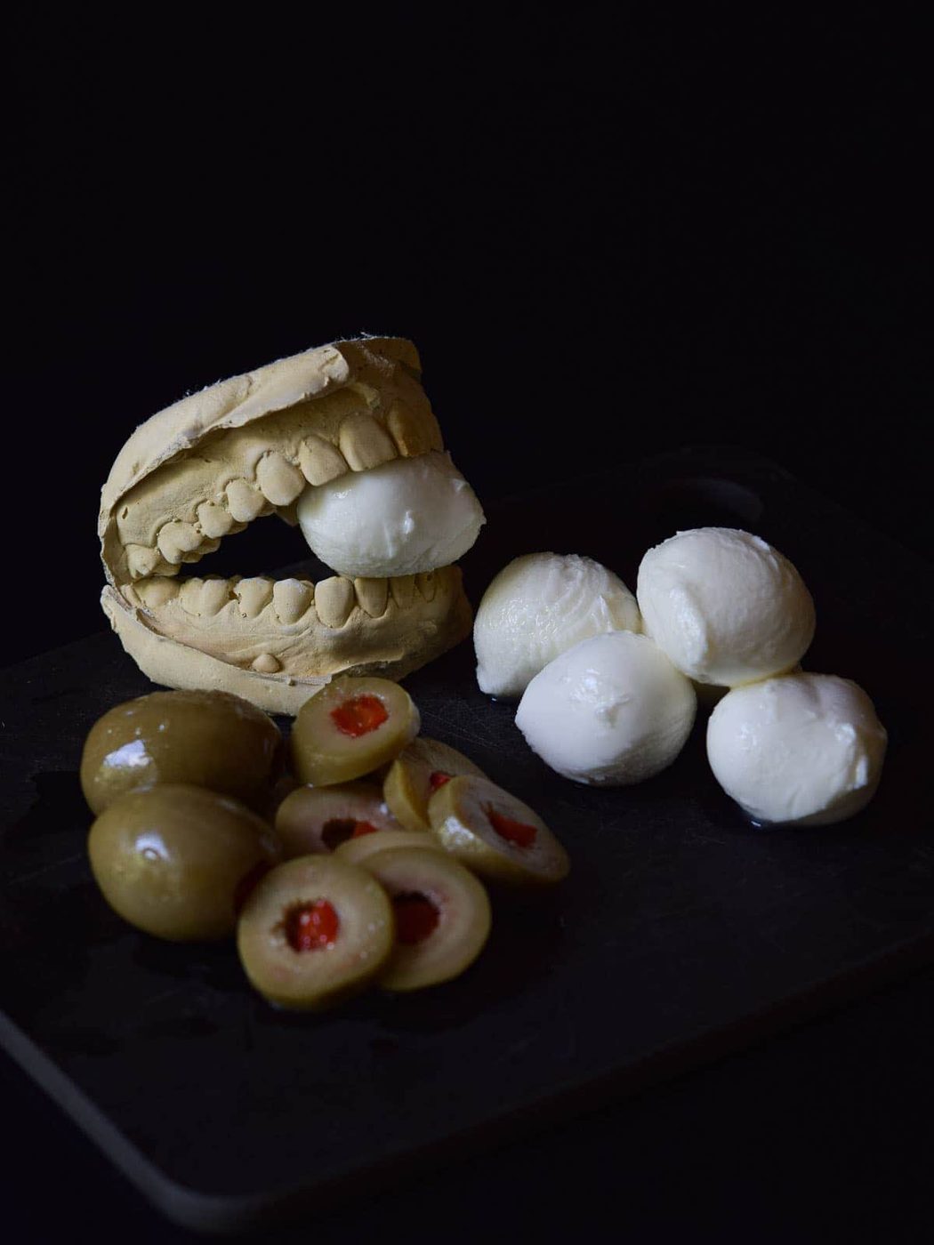 Mozzarella balls with olives on a black surface.