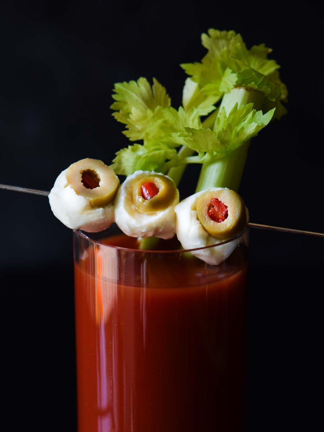 Close up of mozzarella and olives on a cocktail pick resembling eyeballs.