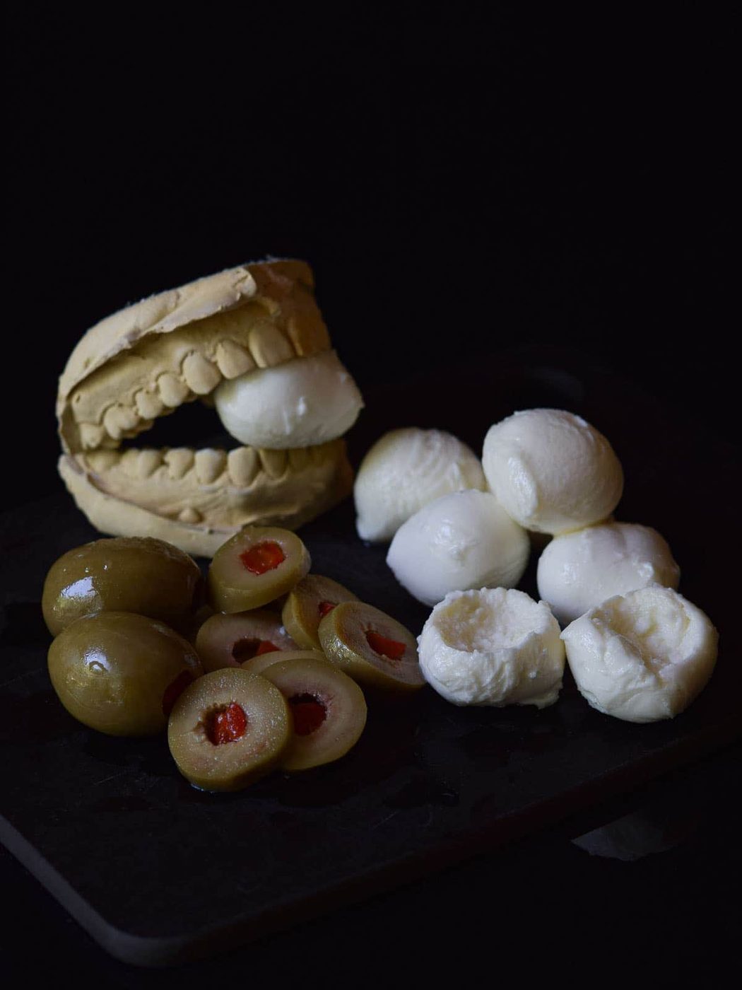 Mozzarella balls with olives, with a scoop taken out on black surface.
