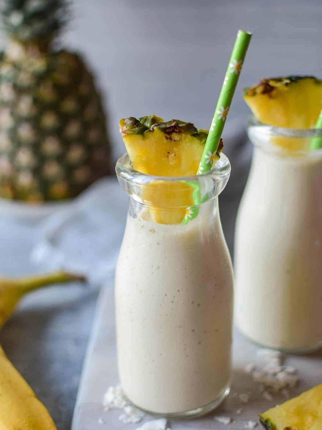 Close-up of banana and pineapple smoothie in a clear glass with a straw.