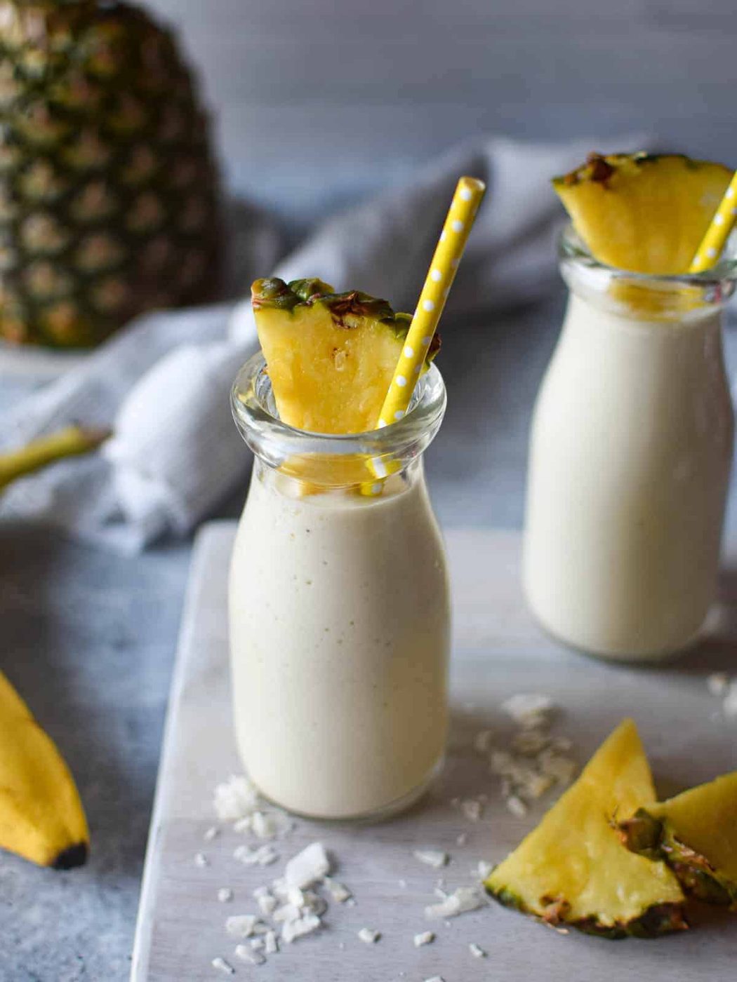 Close-up of banana and pineapple smoothie in a clear glass with a straw.