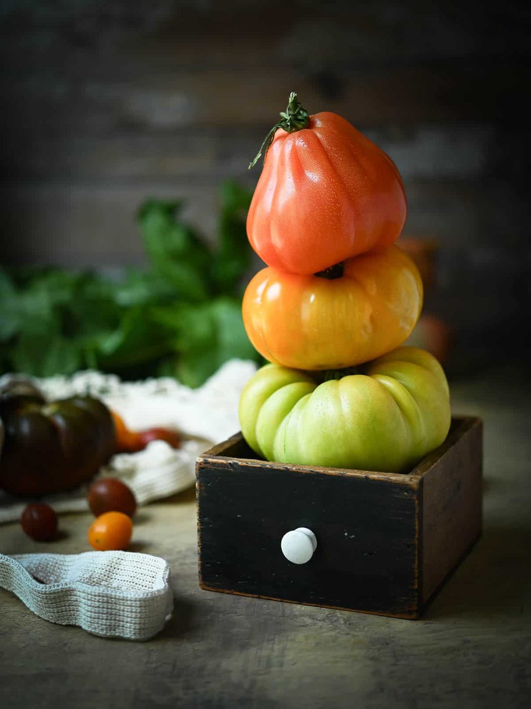 A stack of red, orange, and yellow heirloom tomatoes in a brown vintage box.
