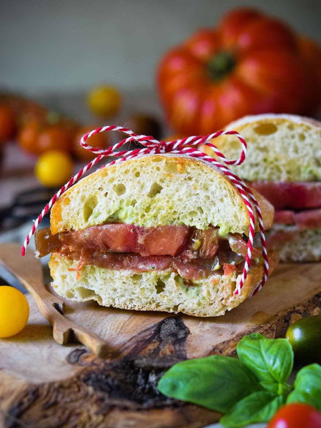 Heirloom tomato and pesto ciabatta roll cut in half on a wood board.