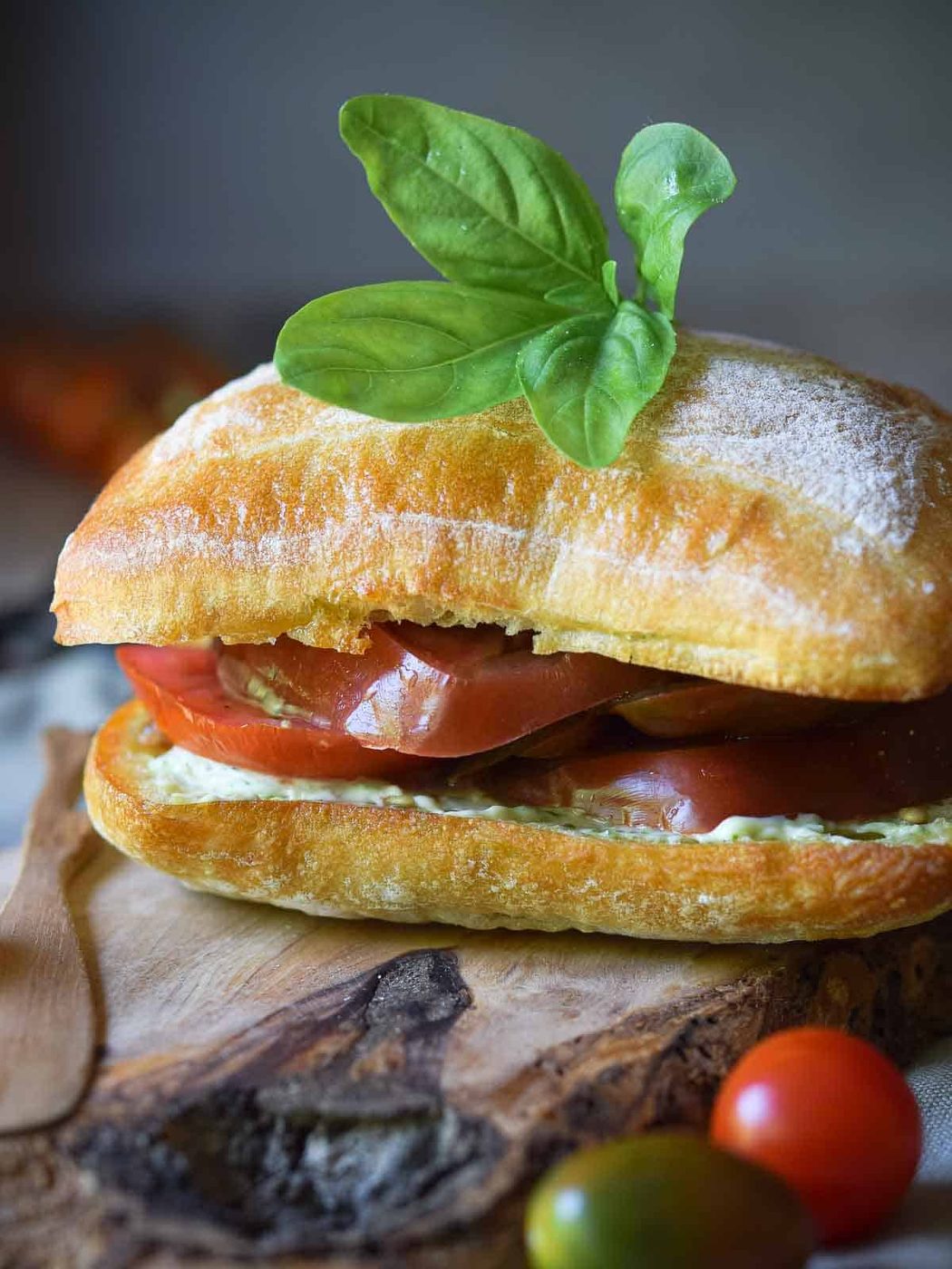 Ciabatta roll with tomatoes and pesto, topped with a few leaves of fresh basil on a wood board.