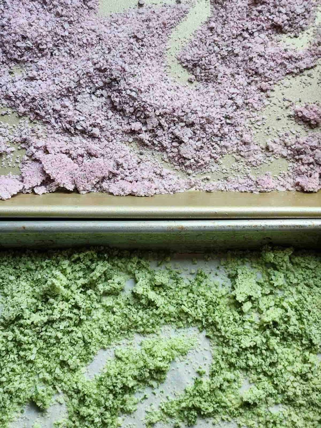 Overhead view of two baking sheets showing dried purple and green basil salt side by side.