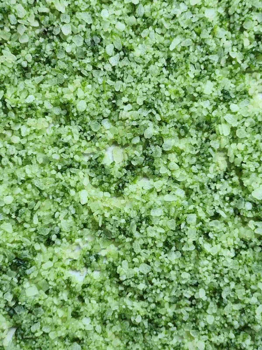 Overhead of green basil salt spread out on a baking sheet.