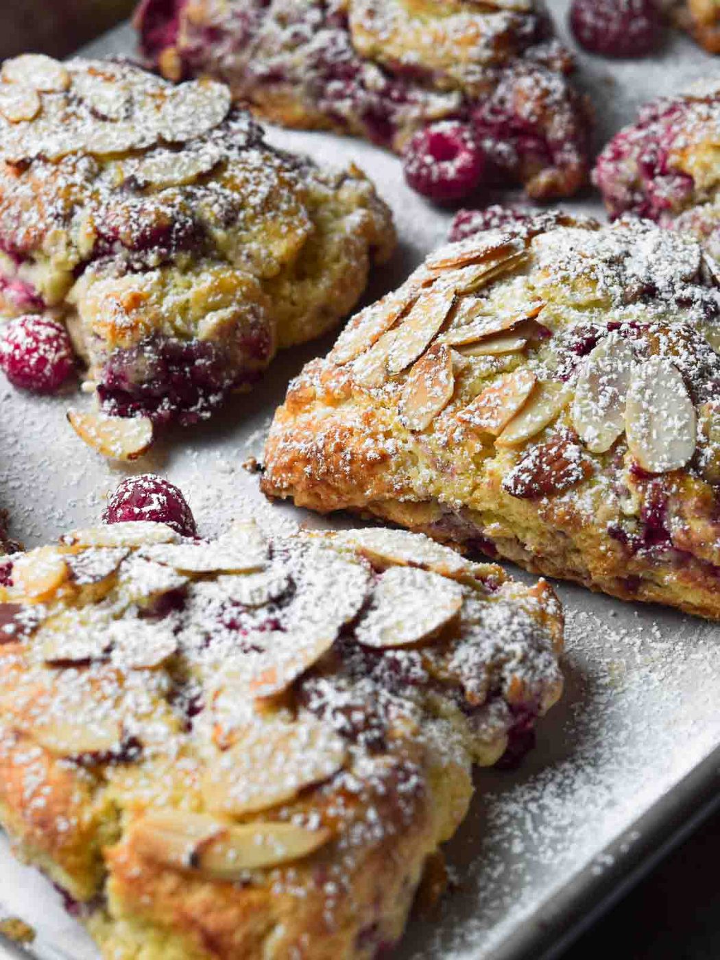 Raspberry almond scones on a baking pan sprinkled with powdered sugar.