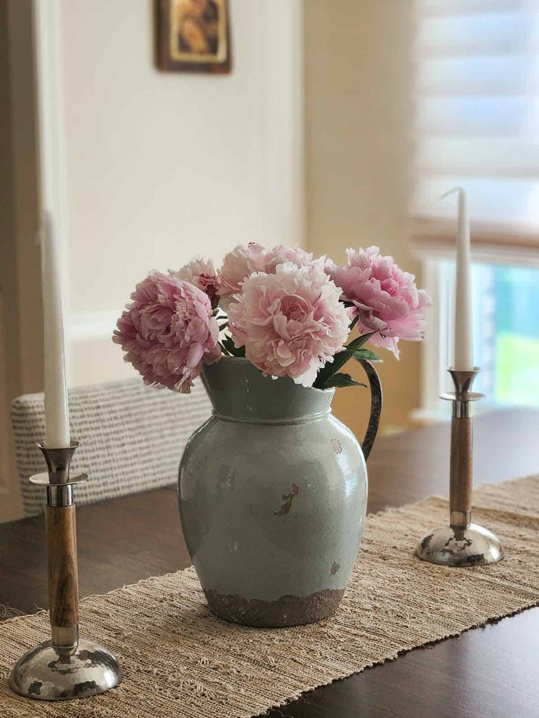 A blue antique pitcher with pink peonies on a wooden table.