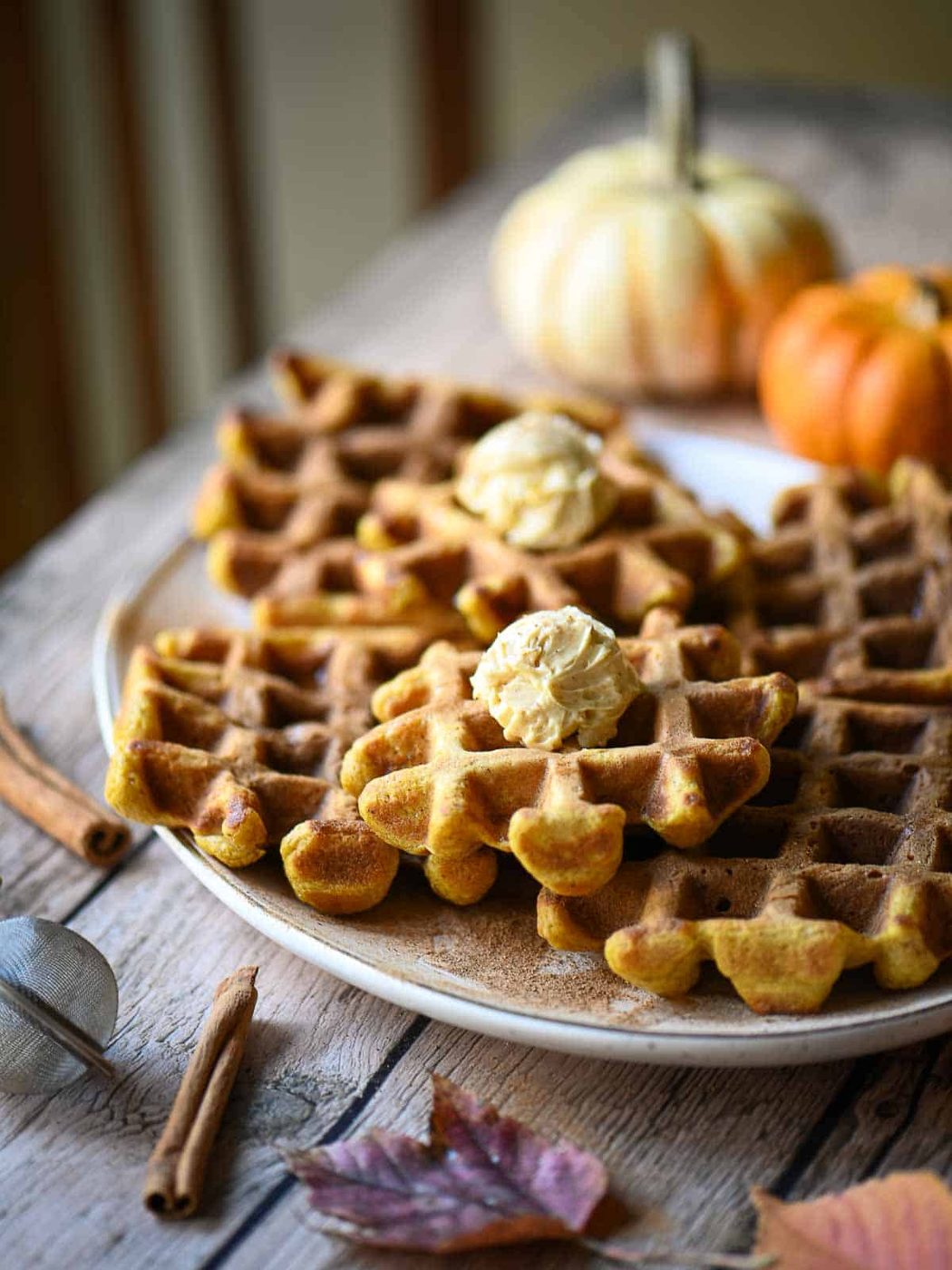 A platter of waffles on a wooden table with pumpkins in the background.