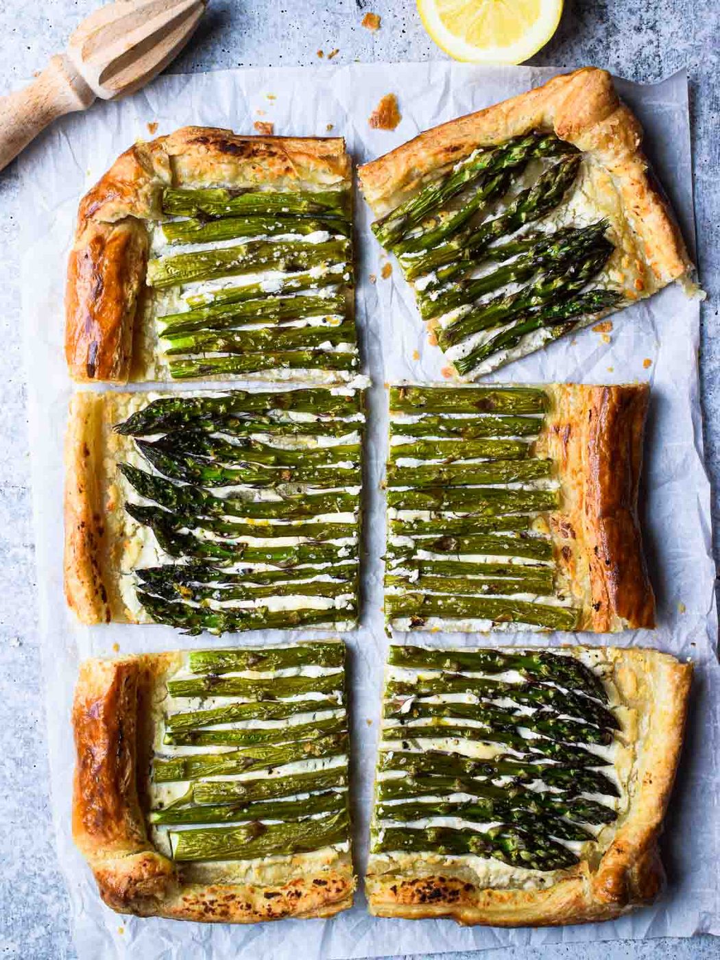 Overhead of asparagus and whipped goat cheese puff pastry tart cut into six pieces with a lemon to the side