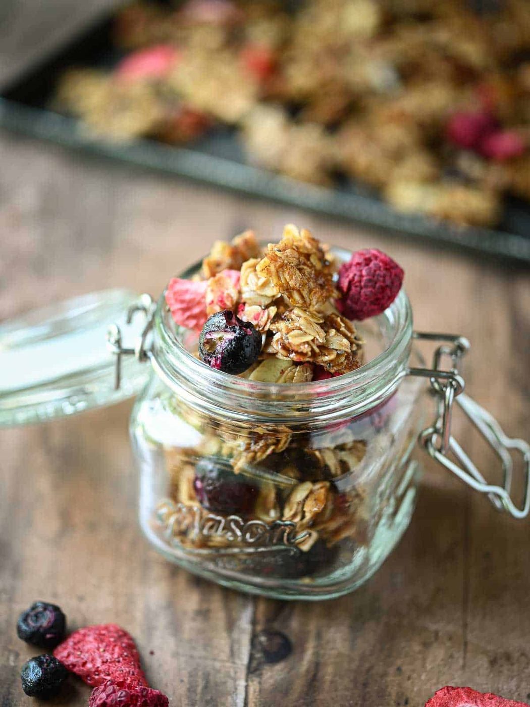 Berry granola in a clear mason jar on a wood surface.