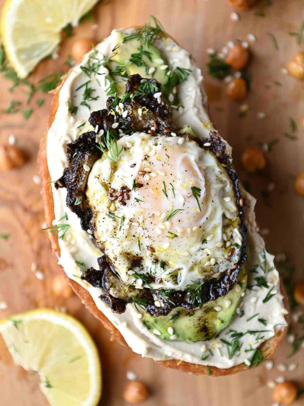 Overhead close-up of hummus on toast with a fried egg, avocado, and dill.