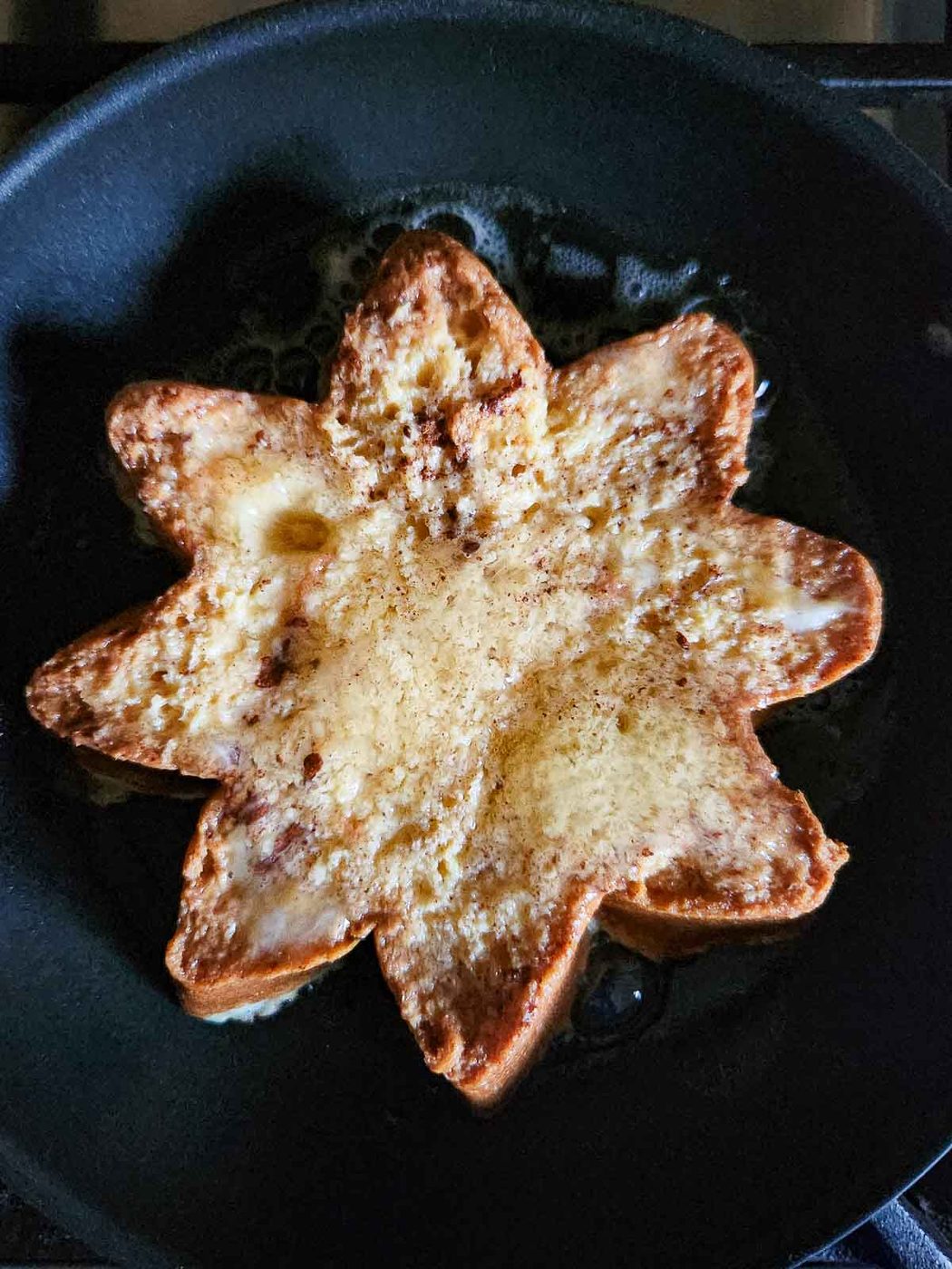 A slice of Pandoro French toast cooking in a black skillet.