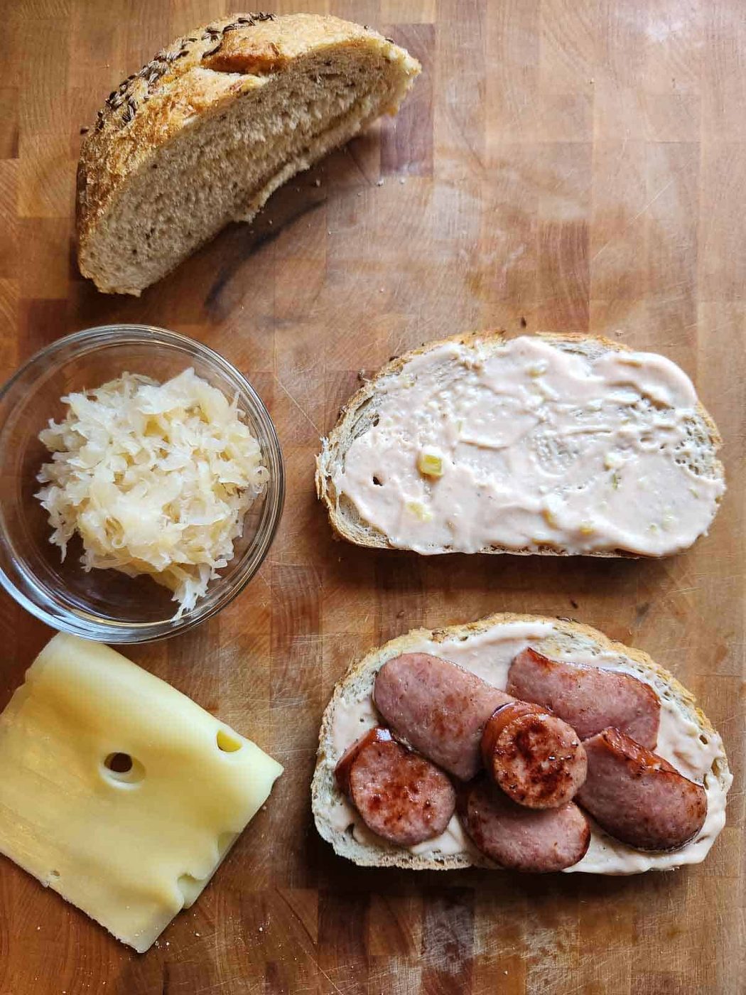 Bread, sauerkraut, meat, and cheese on a cutting board.