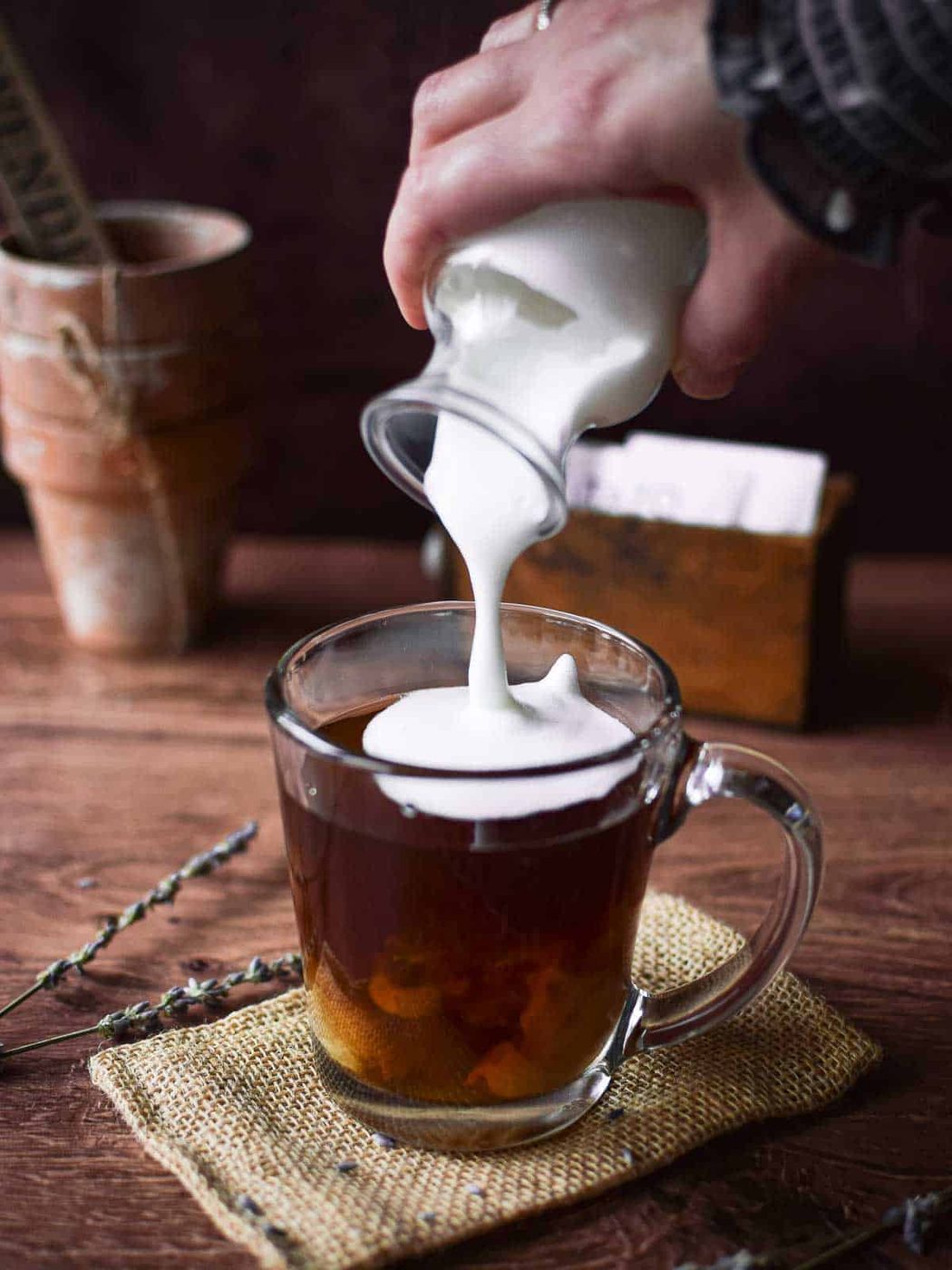 Angled view of frothed milk being poured into a glass with tea to make a lavender tea latte.