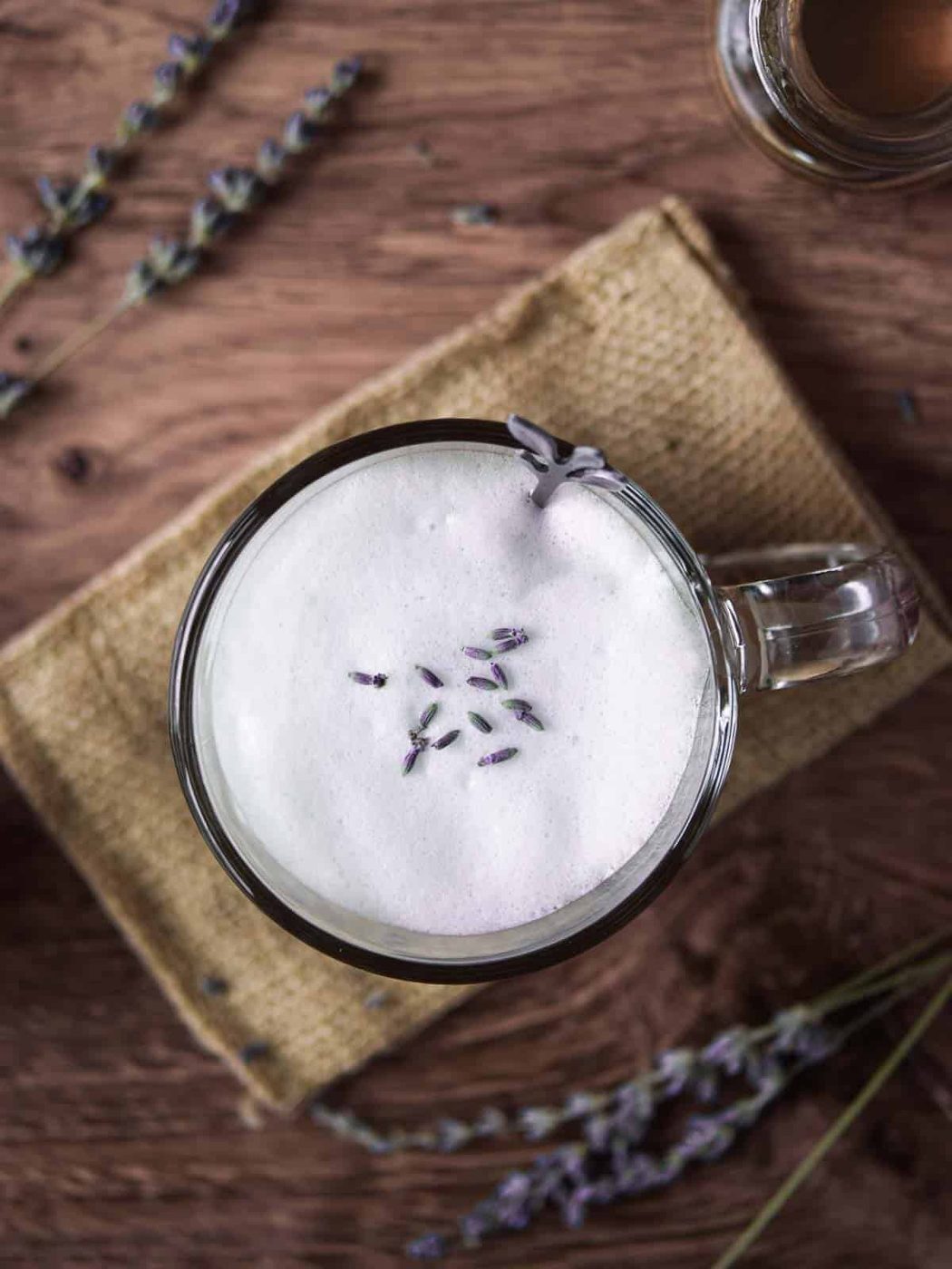 Overhead of a lavender tea latte on a wood background with lavender sprigs.