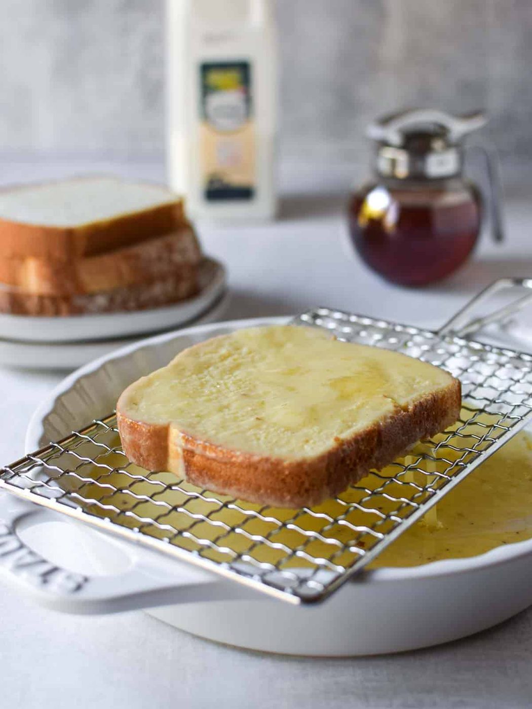 Bread dipped in custard being drained of excess custard over a white bowl.