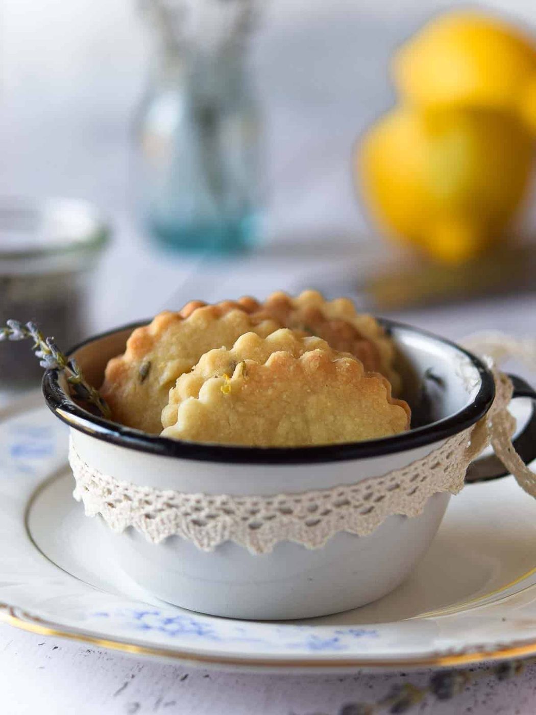 Lemon lavender shortbread cookies in a vintage white enamel cup with lemons in the background.