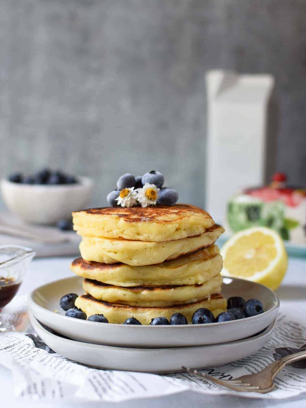 Lemon pancakes stacked on plates with blueberries on top.