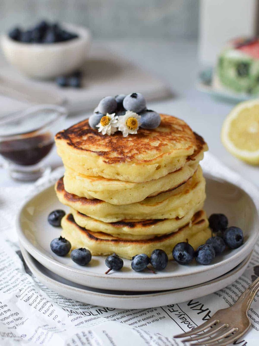 Lemon mascarpone pancakes stacked on plates with blueberries on top.