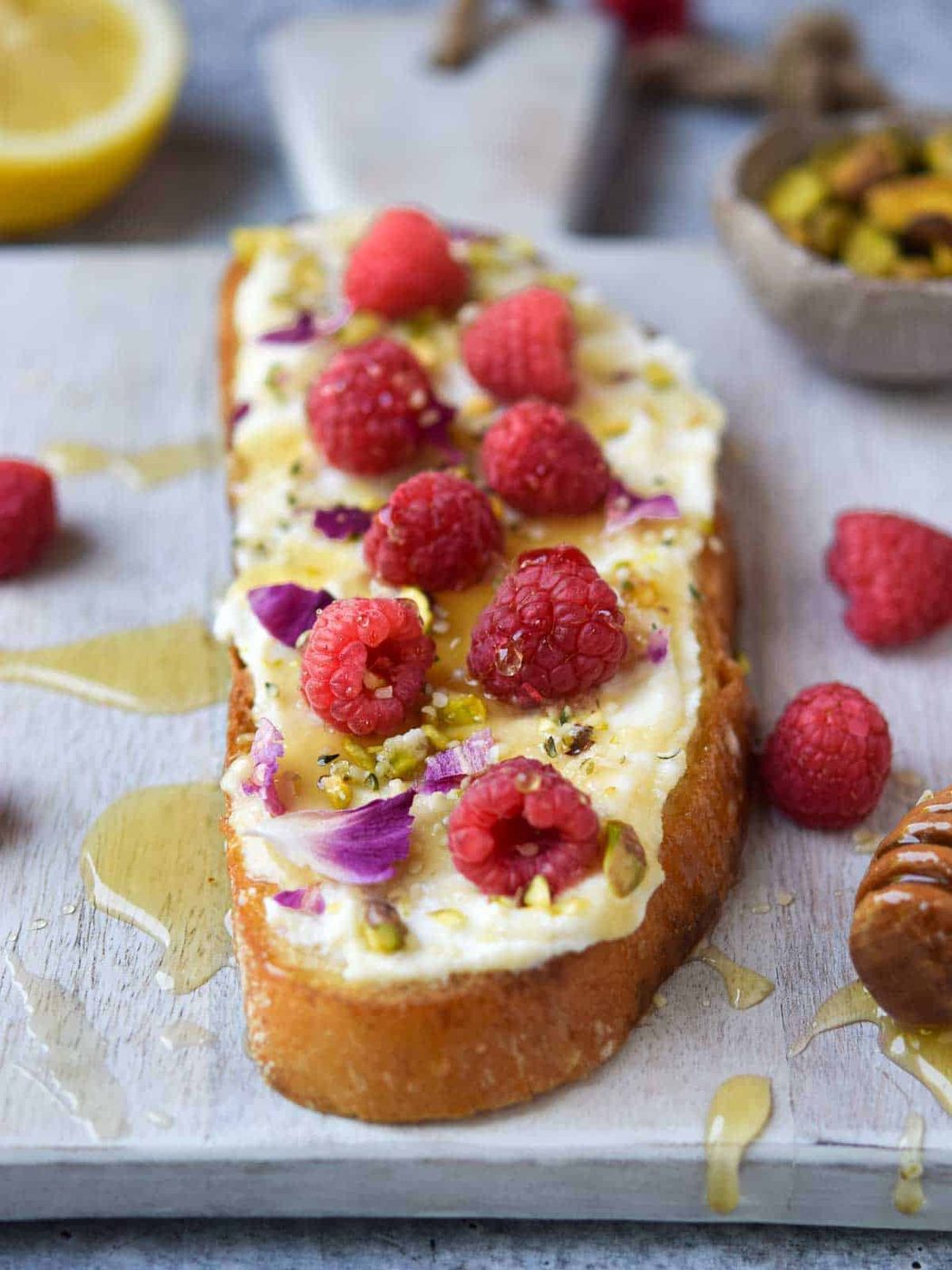 Lemon ricotta raspberry toast with honey drizzled over it on a grey cutting board.
