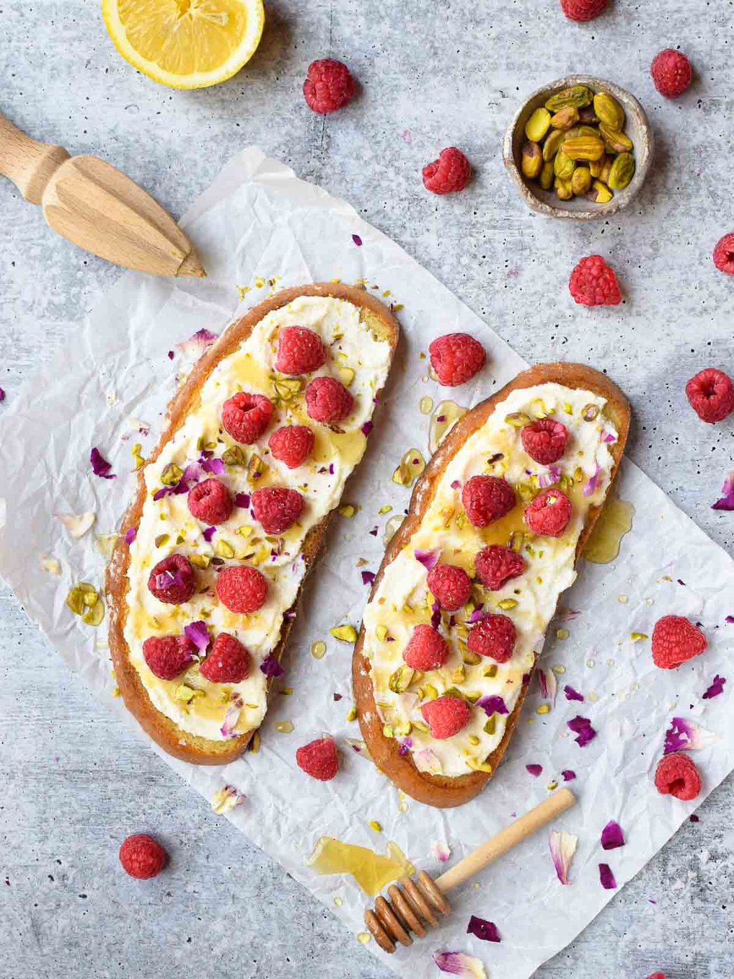 Overhead view of raspberry toast on white parchment paper on a grey surface.
