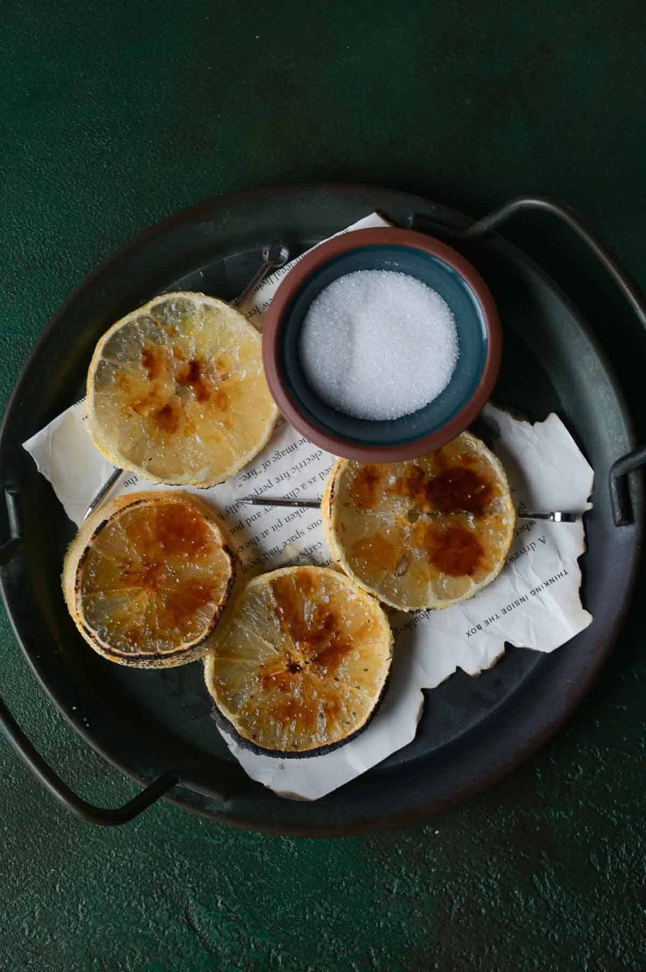 Lemon brûlée slices on a black tray with sugar.