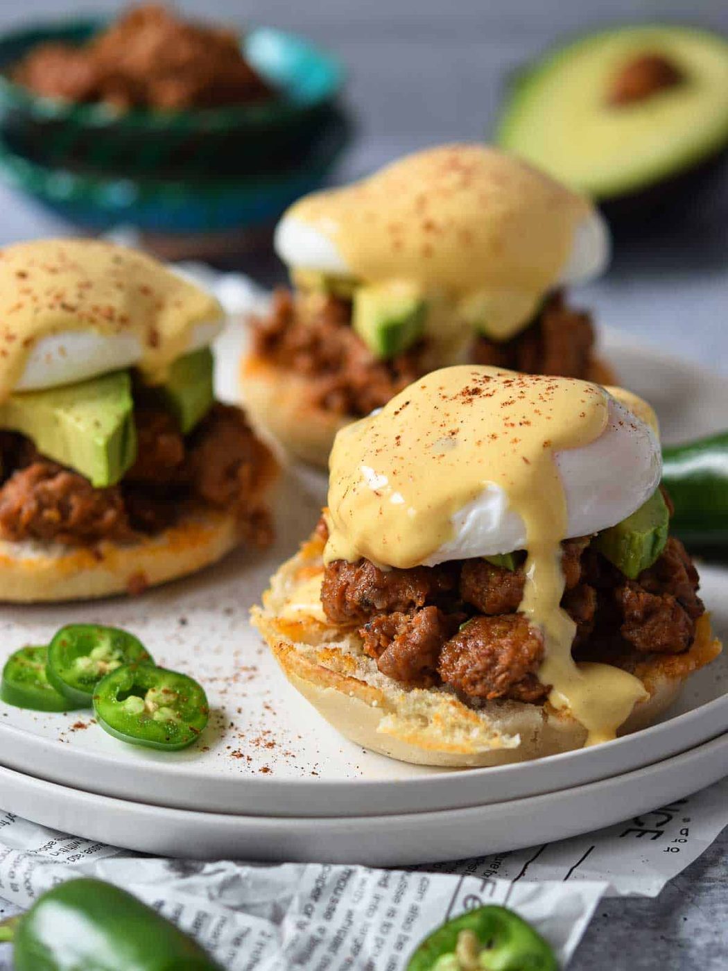 Three eggs benedicts on a white plate with dripping hollandaise sauce.