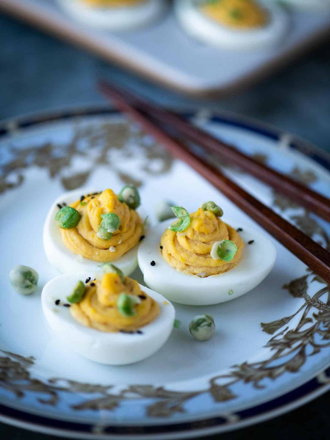 Three deviled eggs on a pretty plate with chopsticks.