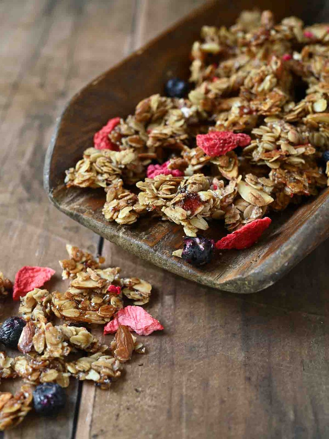 Mixed berry granola falling off a large wooden scoop.