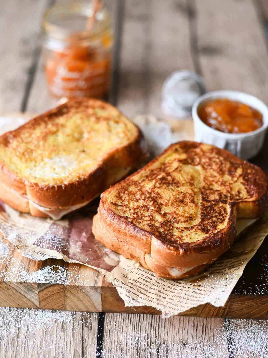 Two Monte Cristo sandwiched on a wooden board with apricot jam.