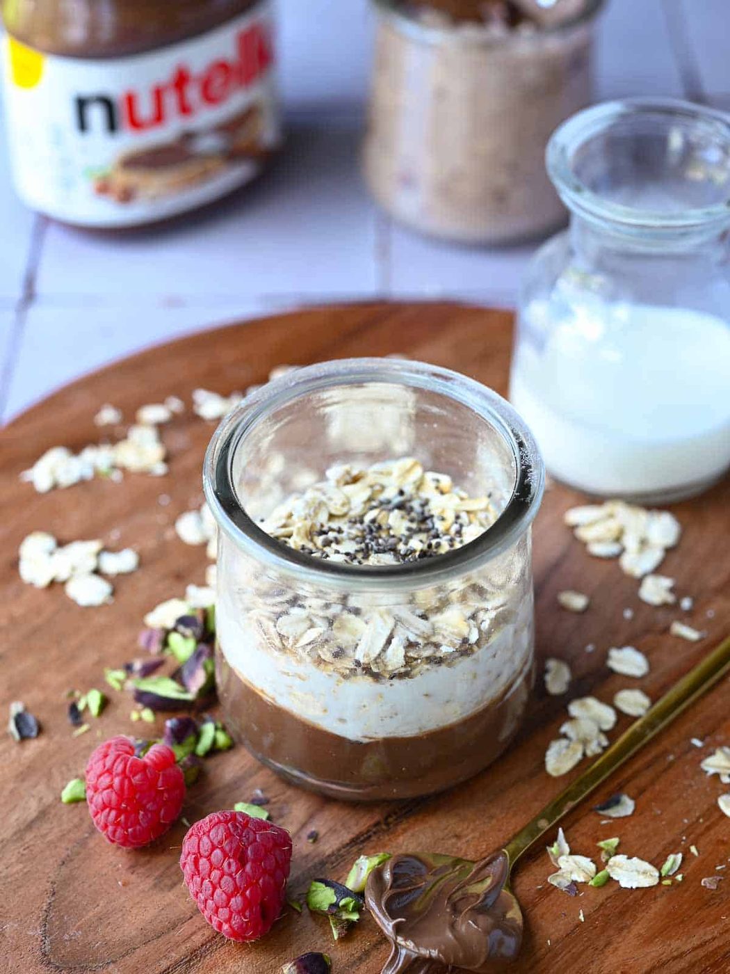 Nutella overnight oats layered in a glass jar with milk in the background.