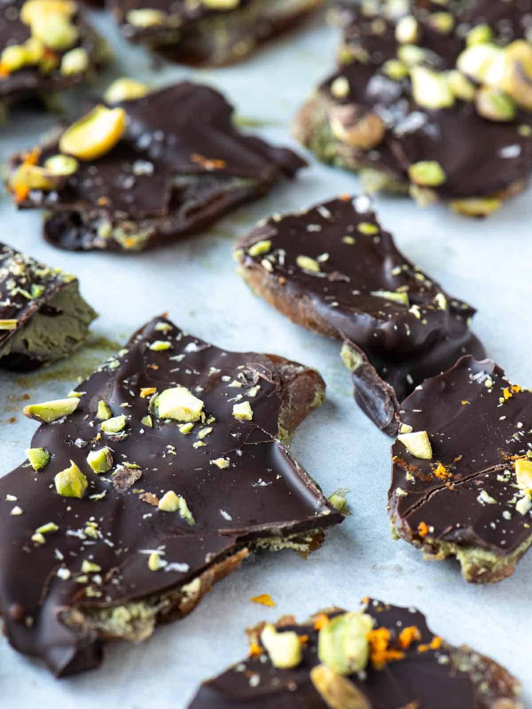 Pieces of orange pistachio date bark on white parchment paper.