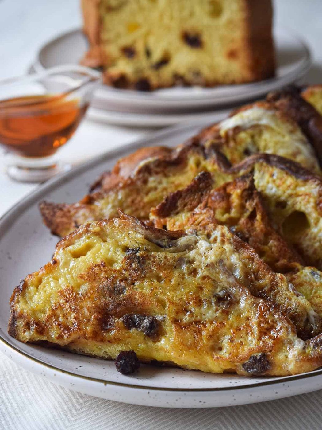 Panettone French toast on a platter with maple syrup and panettone in the background.