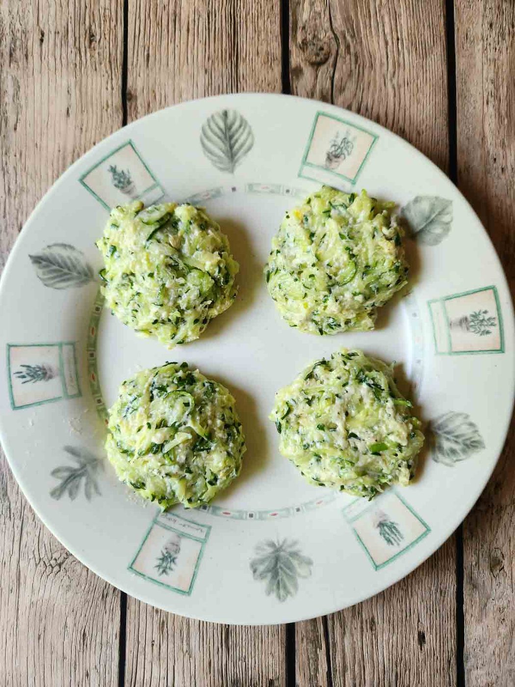 Four uncooked zucchini patties on a plate.