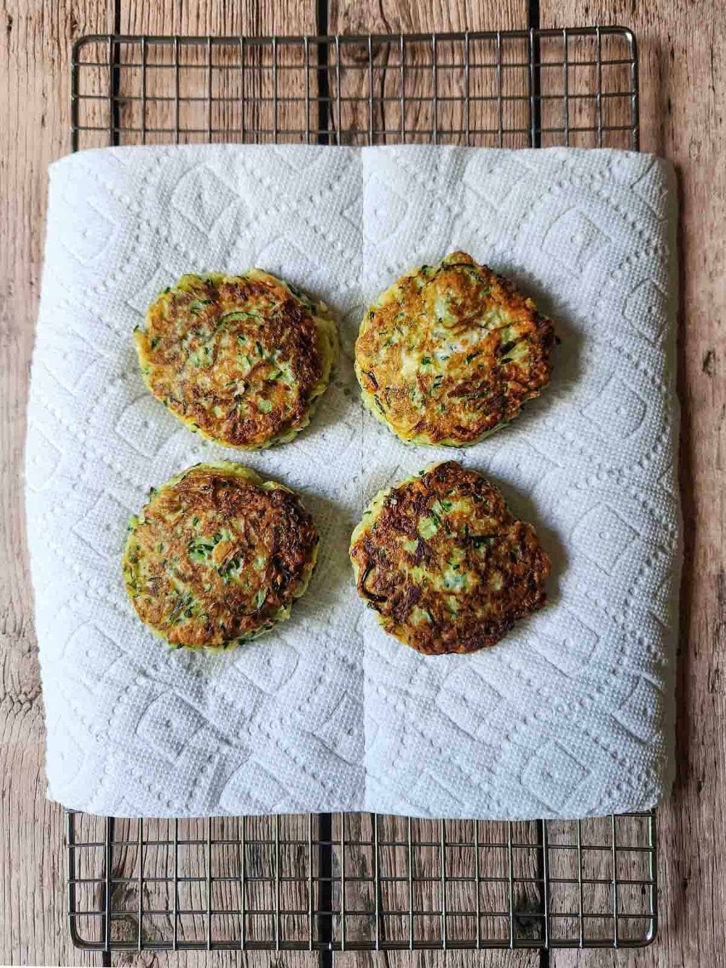 Four cooked zucchini pancakes on a wire rack.