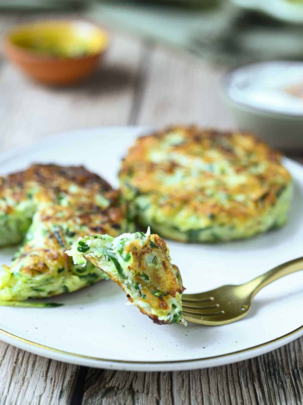 Two zucchini fritters on a plate with a forkful taken out.