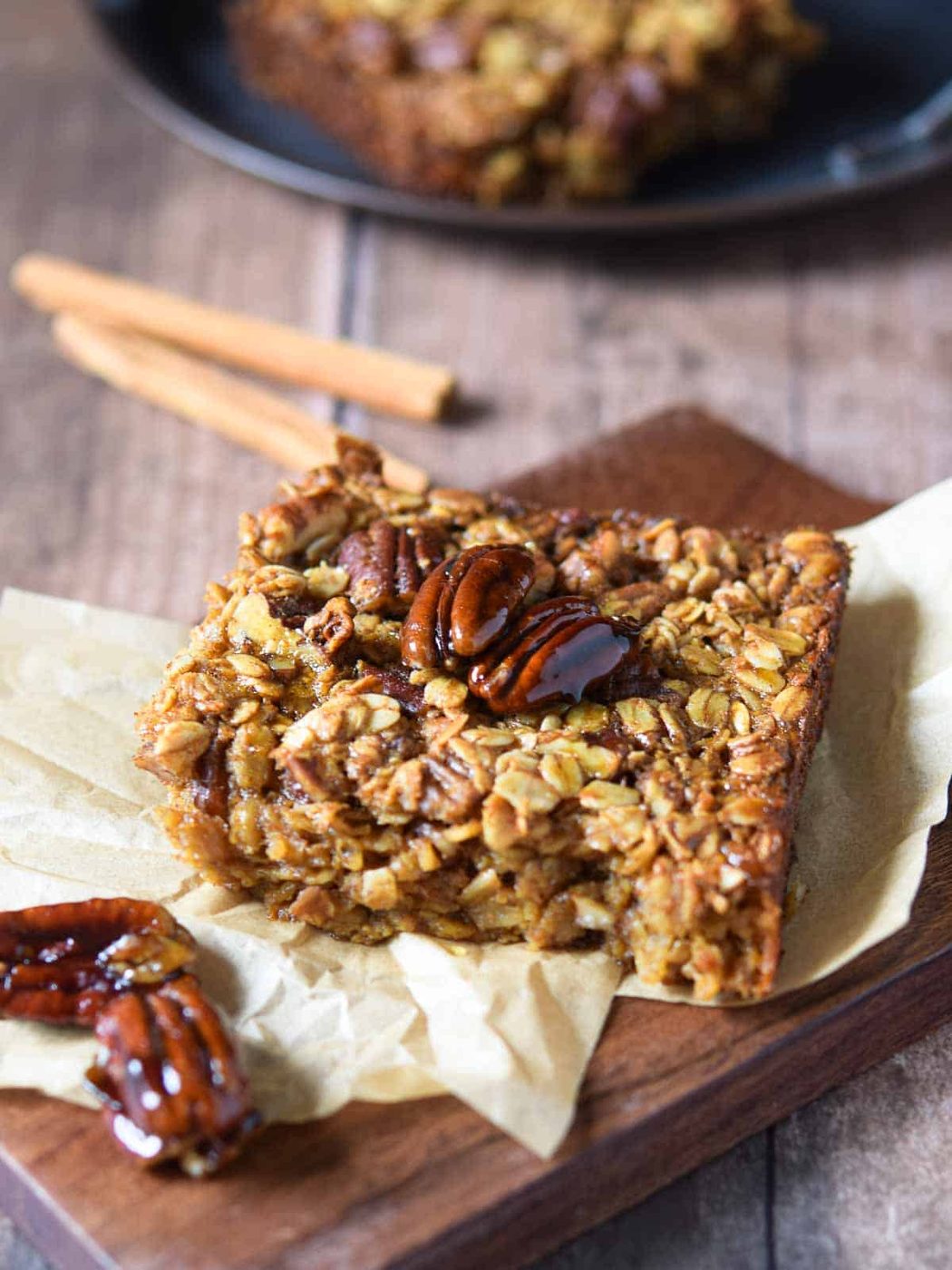 Baked pecan pie oatmeal on a wood slab with cinnamon sticks in the background.