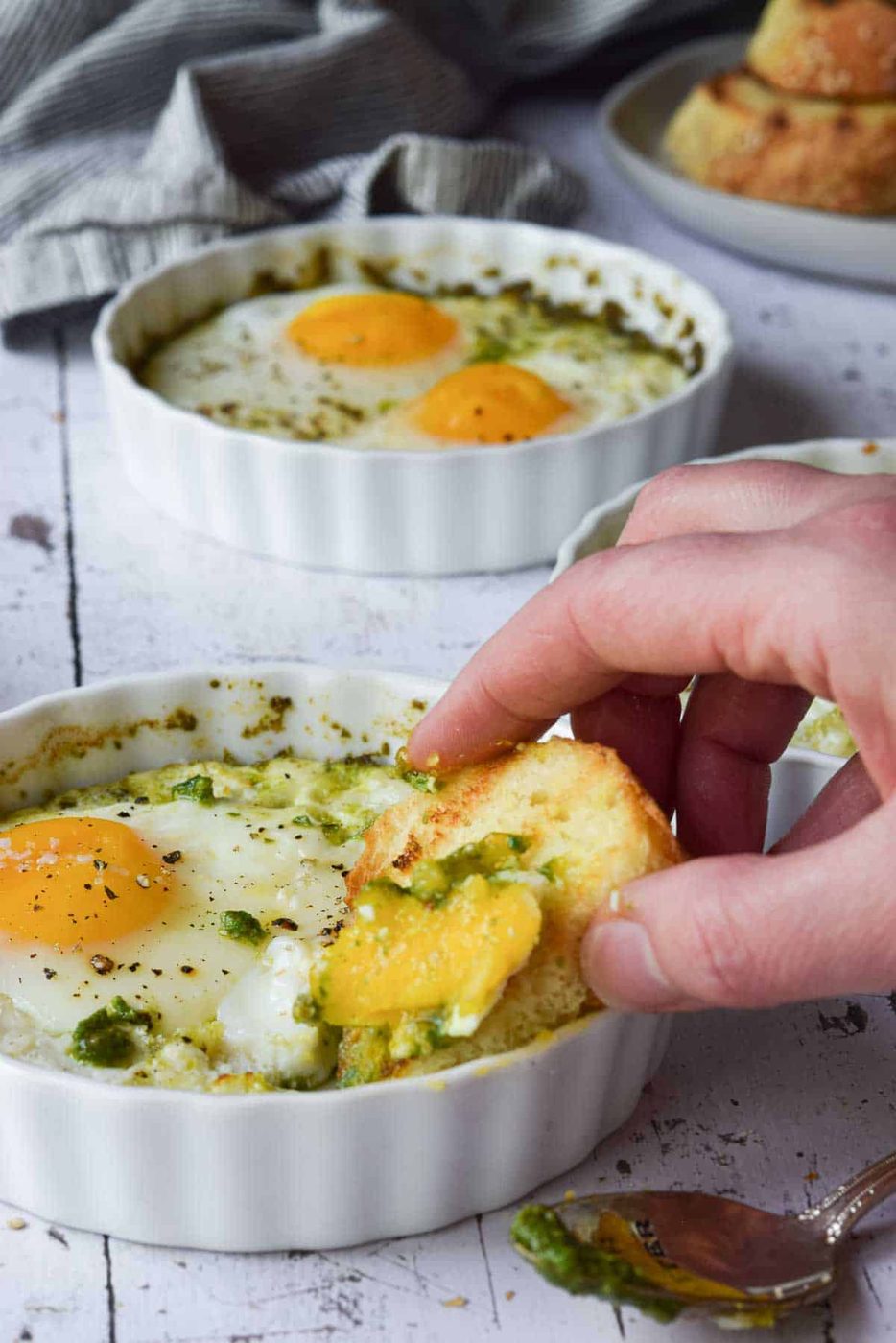 Bread being dunked in baked eggs in a ramekin.