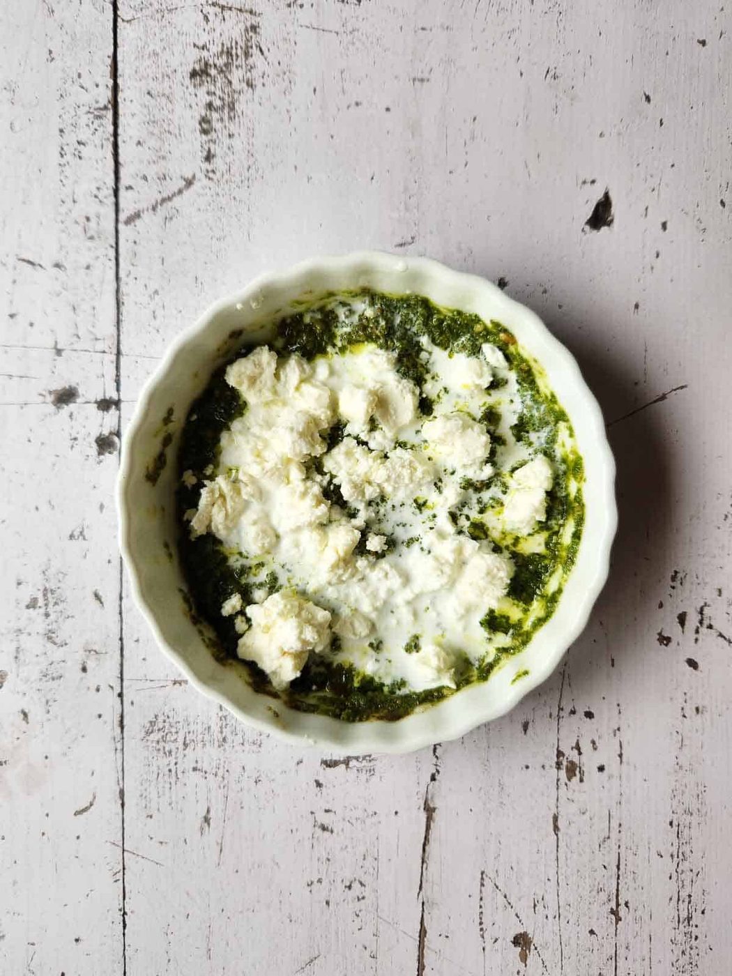 Pesto sauce, feta and cream in a white ramekin.