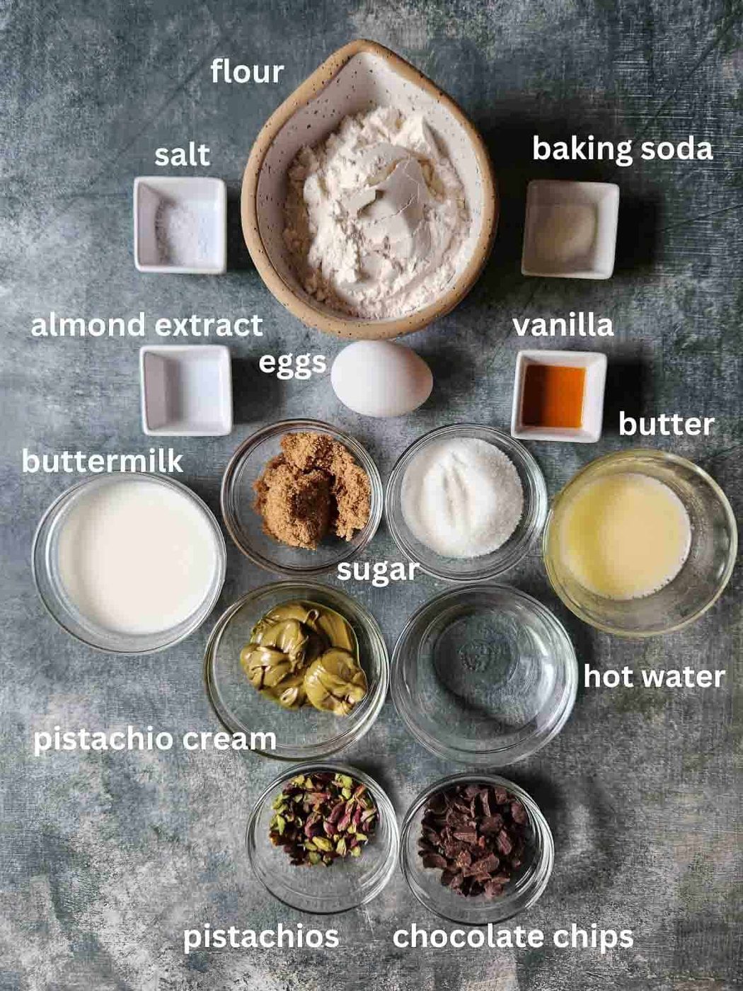 Overhead of ingredients for pistachio muffins on a grey surface.