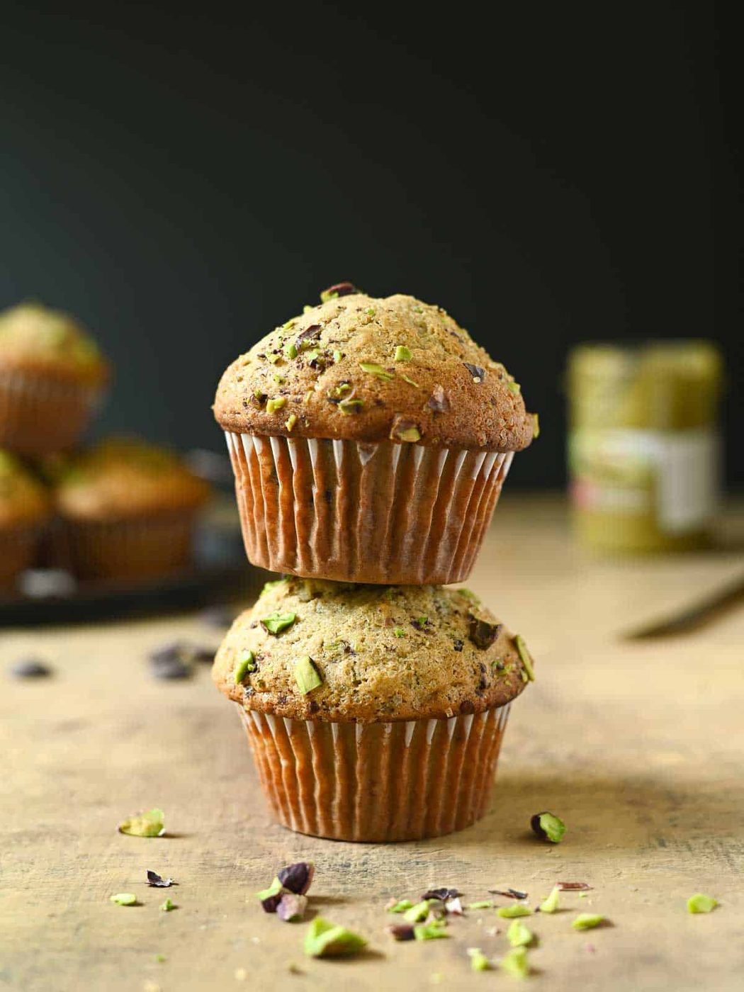 Two pistachio muffins stacked on top of each other on a brown surface.