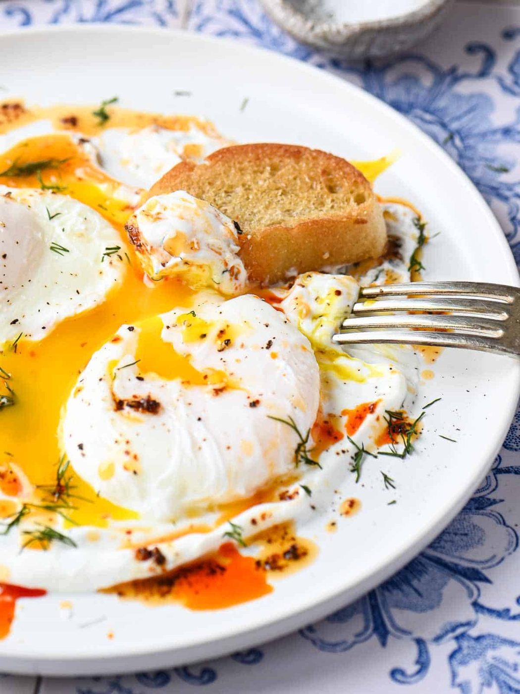 Poached eggs on a white dish with toasted bread and a fork.